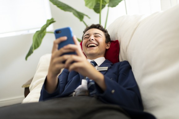 Person in a suit laughs while using a smartphone.