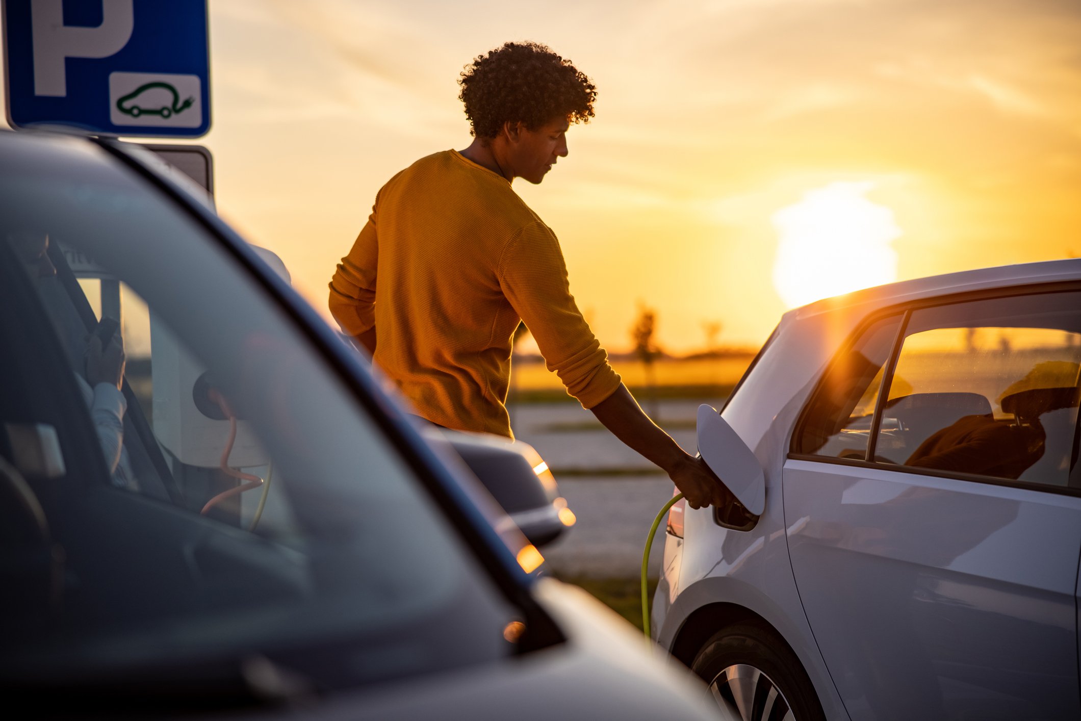 A person charges an electric vehicle at sunset.