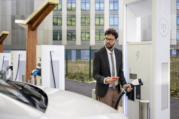 A person uses their phone at a charging station to charge a vehicle. 