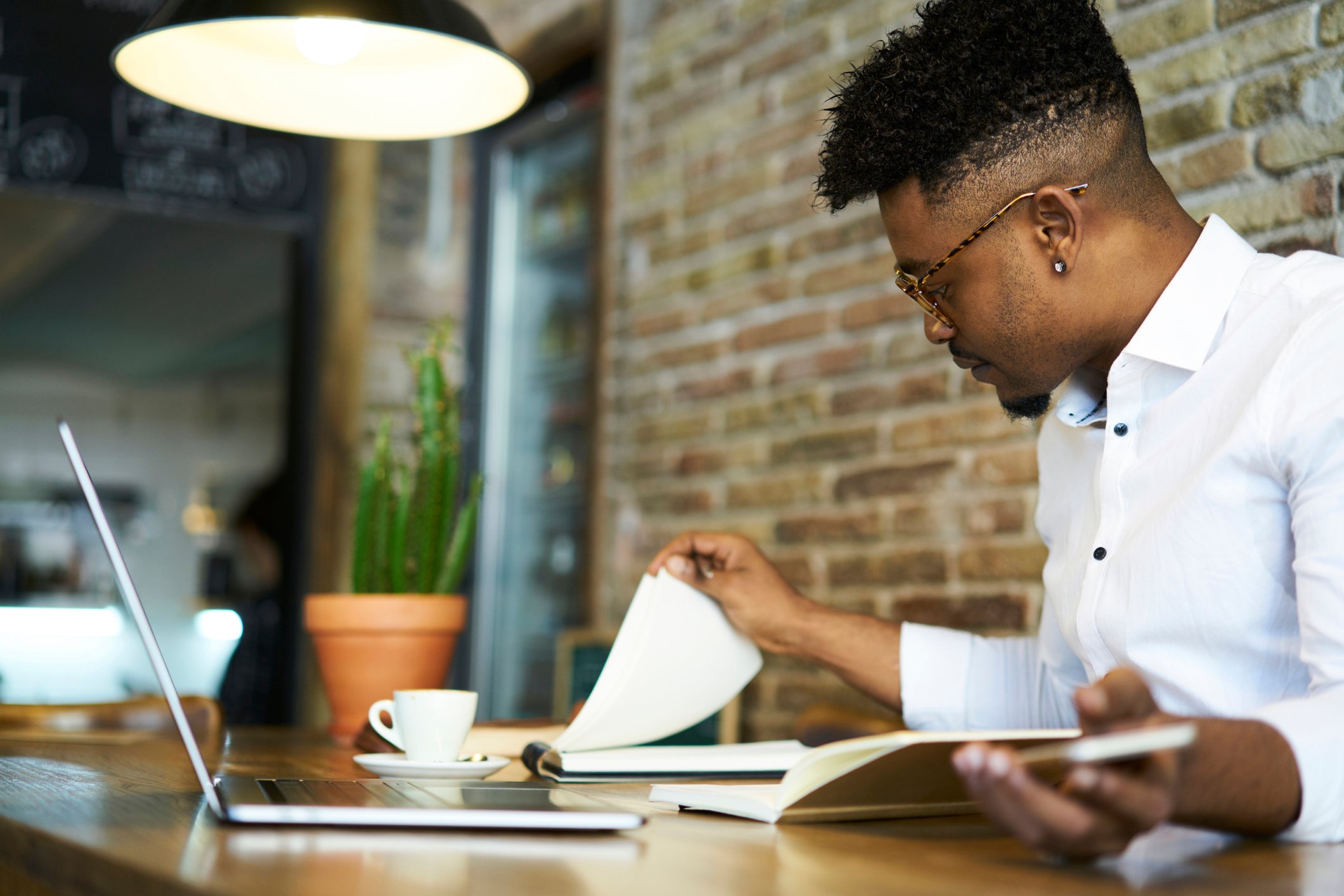 A person at a cafe table looks at some papers and a laptop.