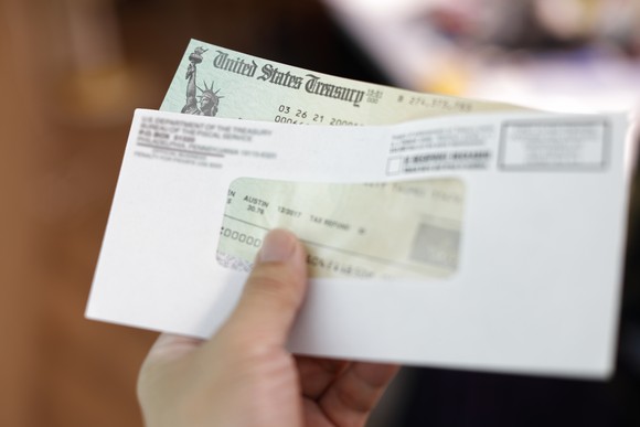 A hand holding a U.S. Treasury tax refund check and envelope.