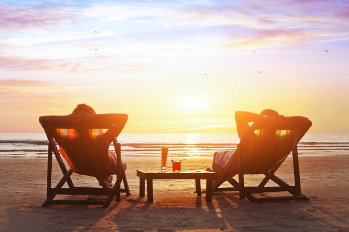 Two people lying on lounge chairs on a beach  while looking at the sunset.