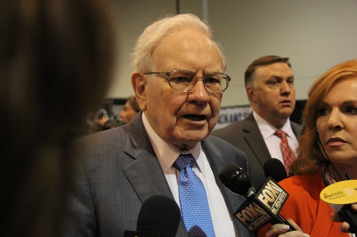 Warren Buffett at an event speaking into a microphone.