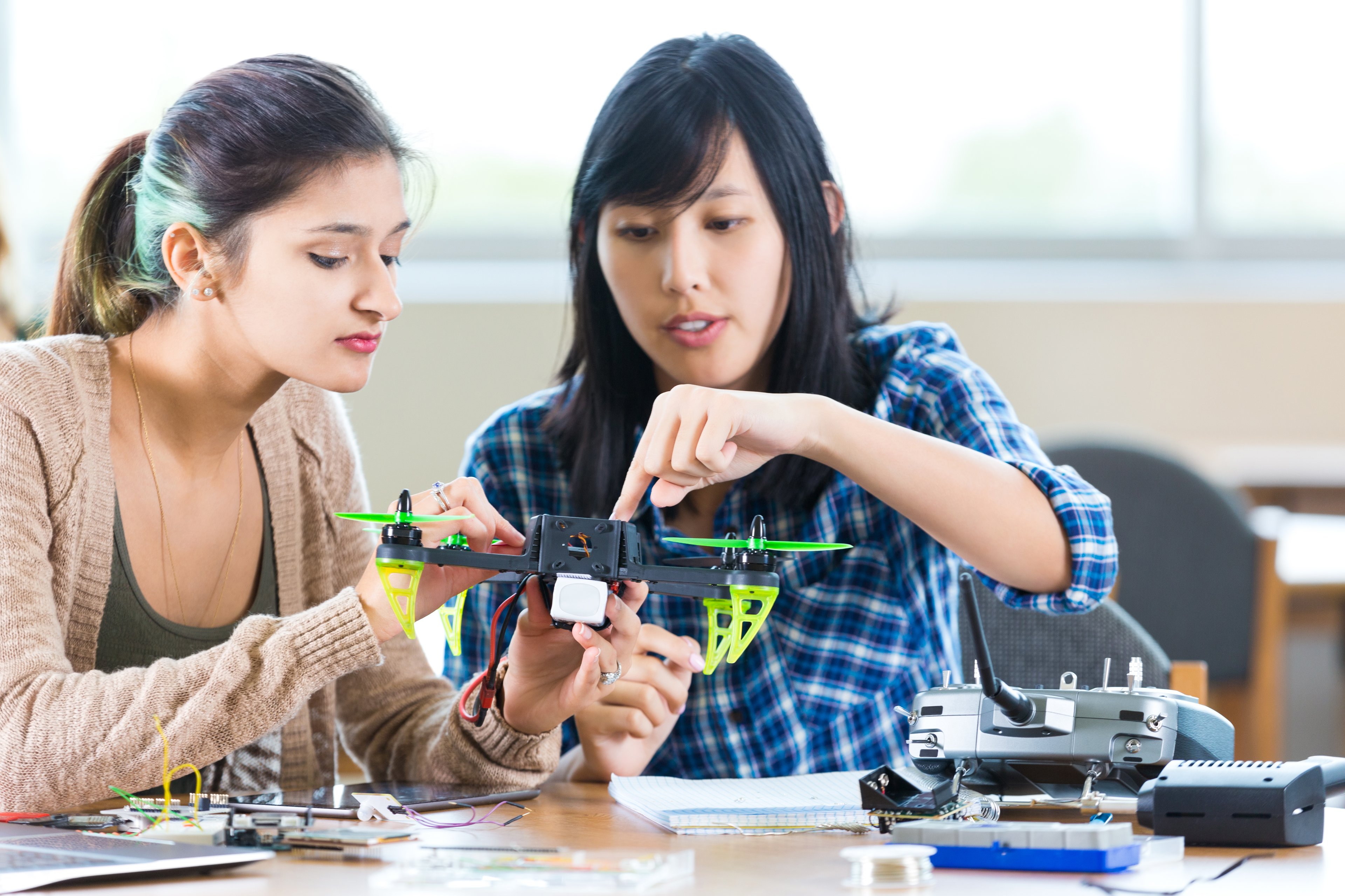 Two people sitting at a desk working on a drone.