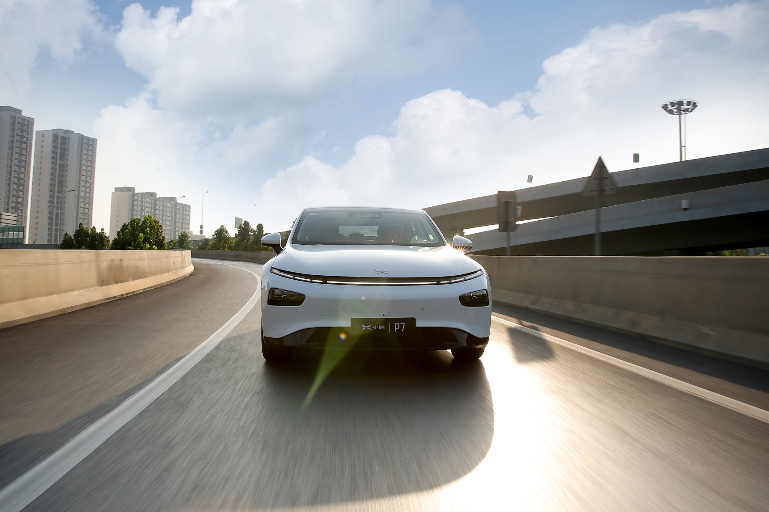 A white XPeng EV sedan on an urban freeway.