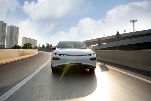 A white XPeng EV sedan on an urban freeway.