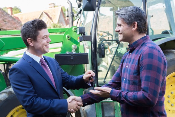 A person hands the keys to a buyer of a tractor. 