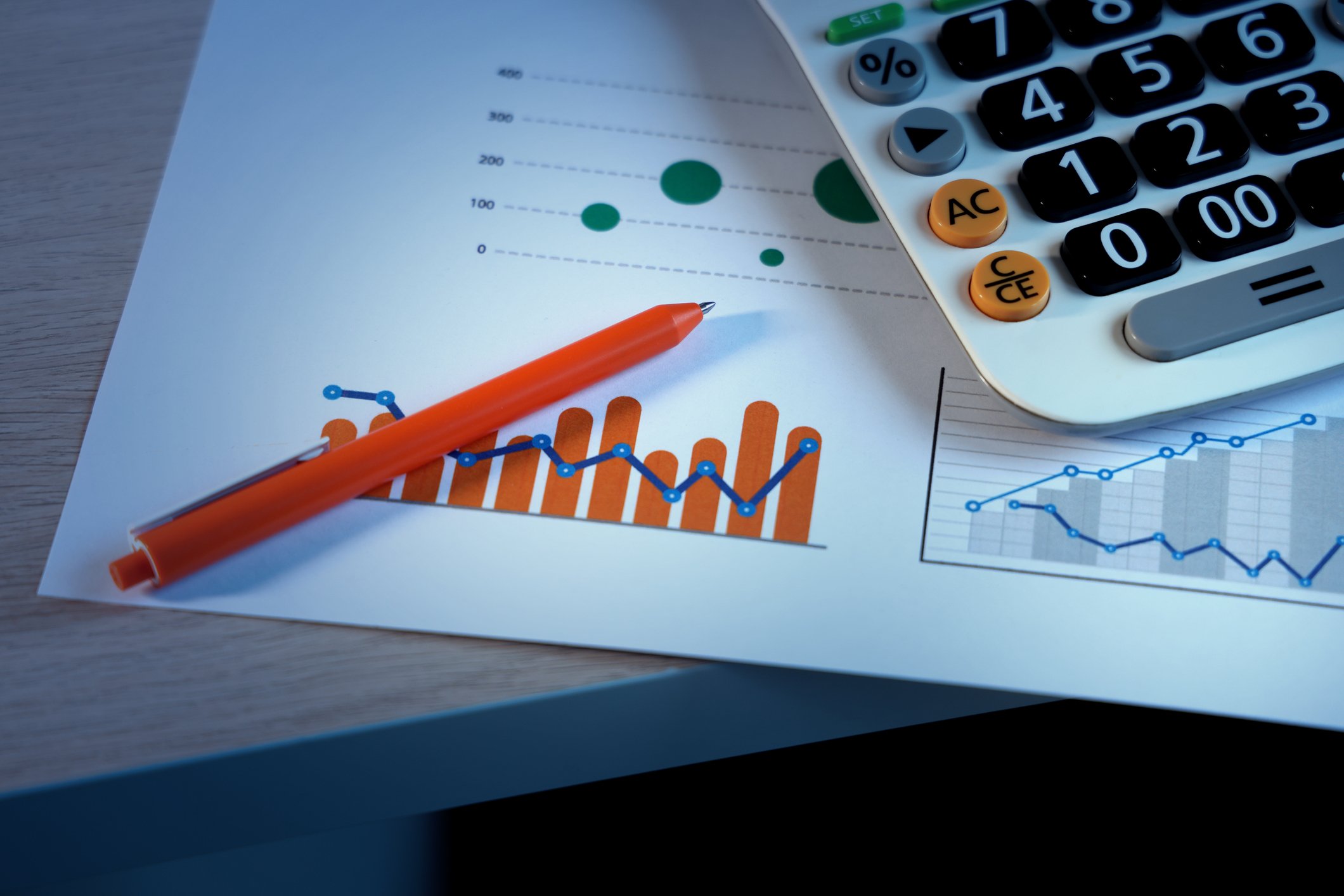A red pen and a calculator sit atop a document showing financial charts.