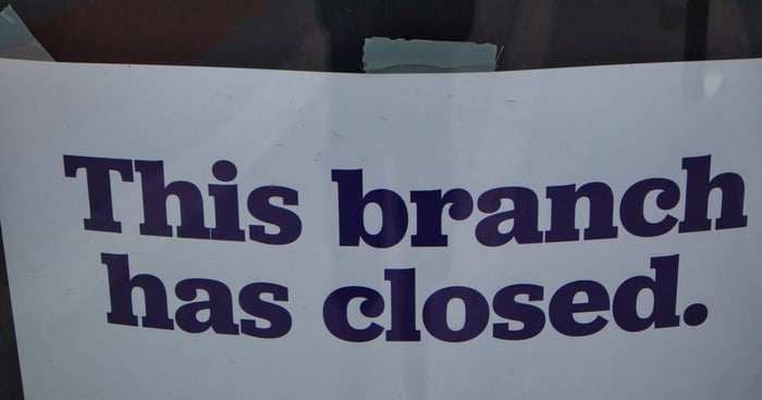 Paper sign on a glass door indicating that a bank has closed permanently.