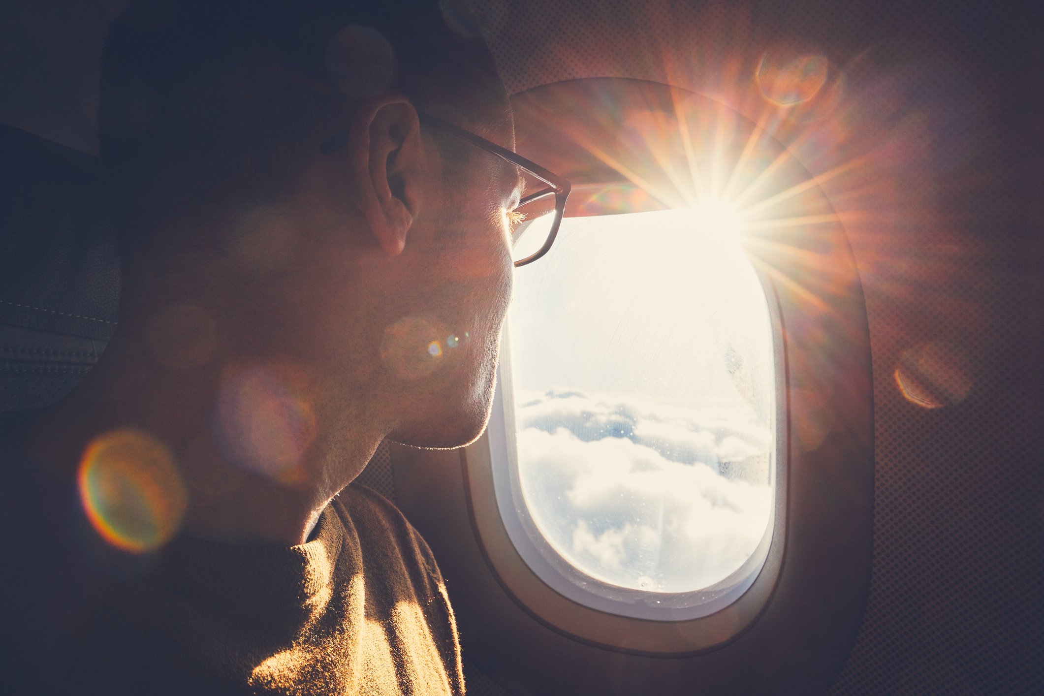 A person looking through an airplane window with sun rays coming in. 