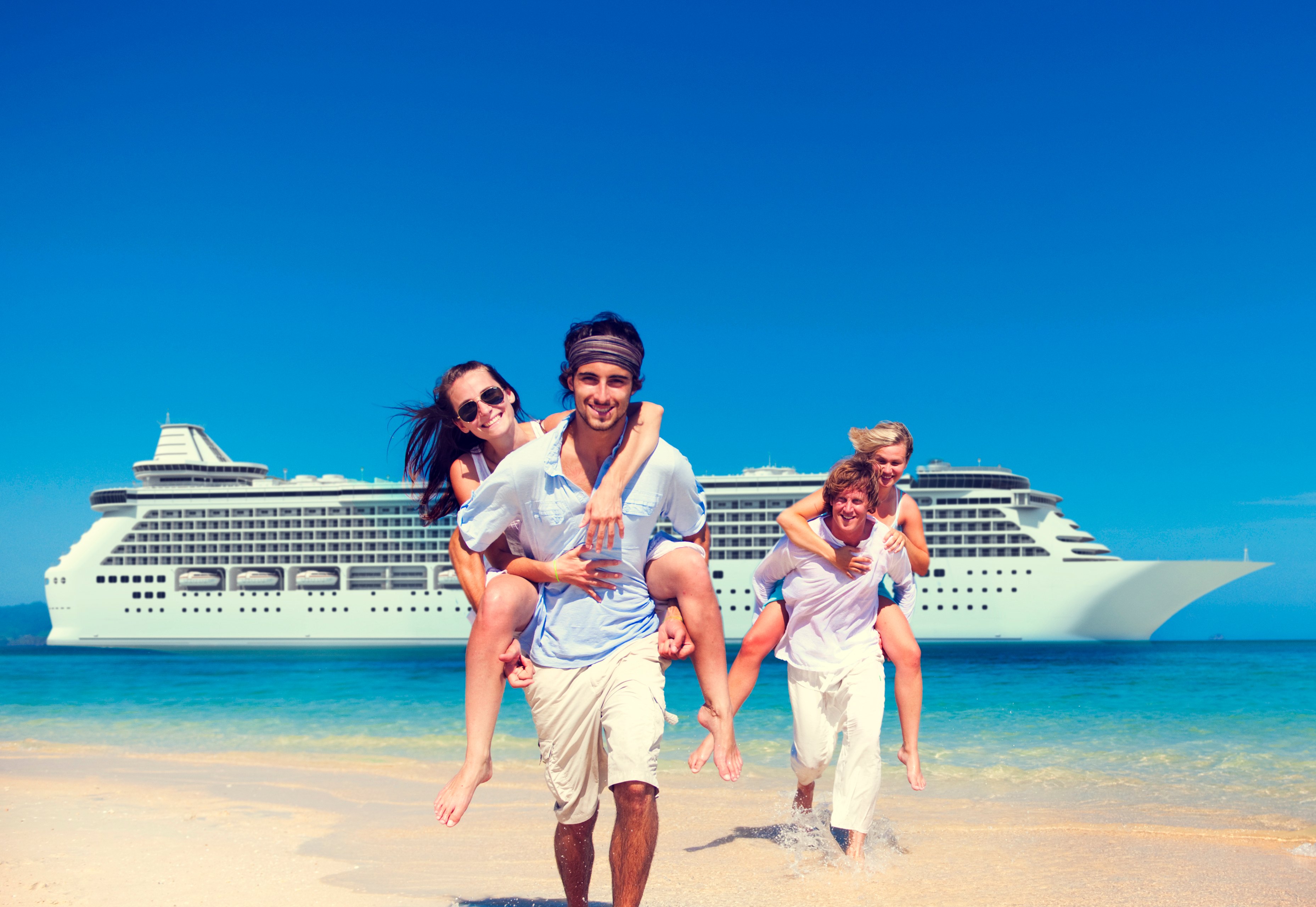 Two couples take photos on a beach with a cruise ship in the background.