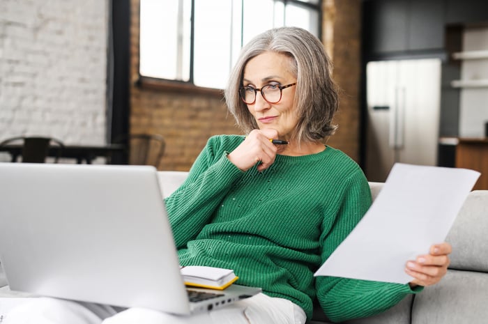 A retired person looking at a screen, deep in thought. 