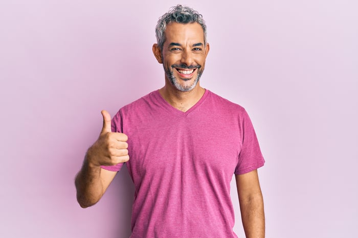 Someone in a pink shirt is making a thumbs-up gesture and smiling.