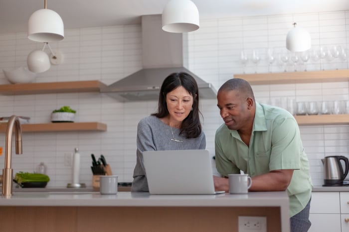 Couple researching on computer in kitchen. 