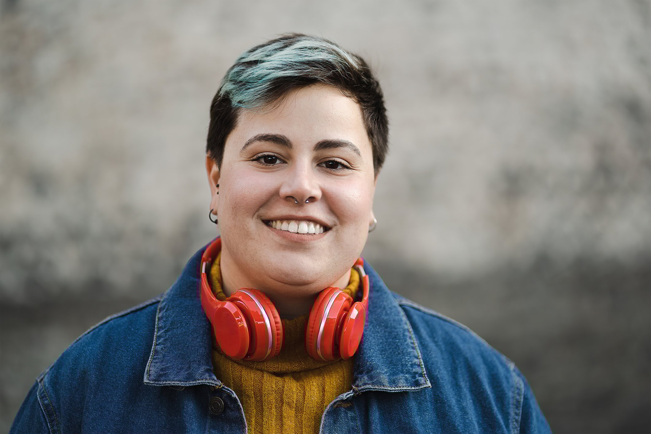 Person outdoors, smiling, with headphones resting on neck.