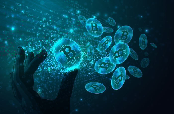 Hand reaching out to hold blue digital Bitcoins.