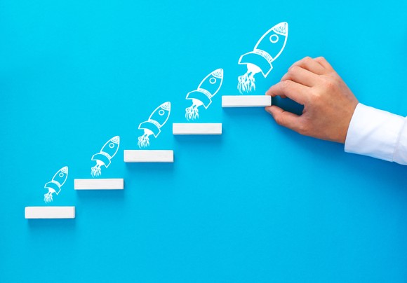 A hand drawing rockets in a stepwise manner against a blue background.