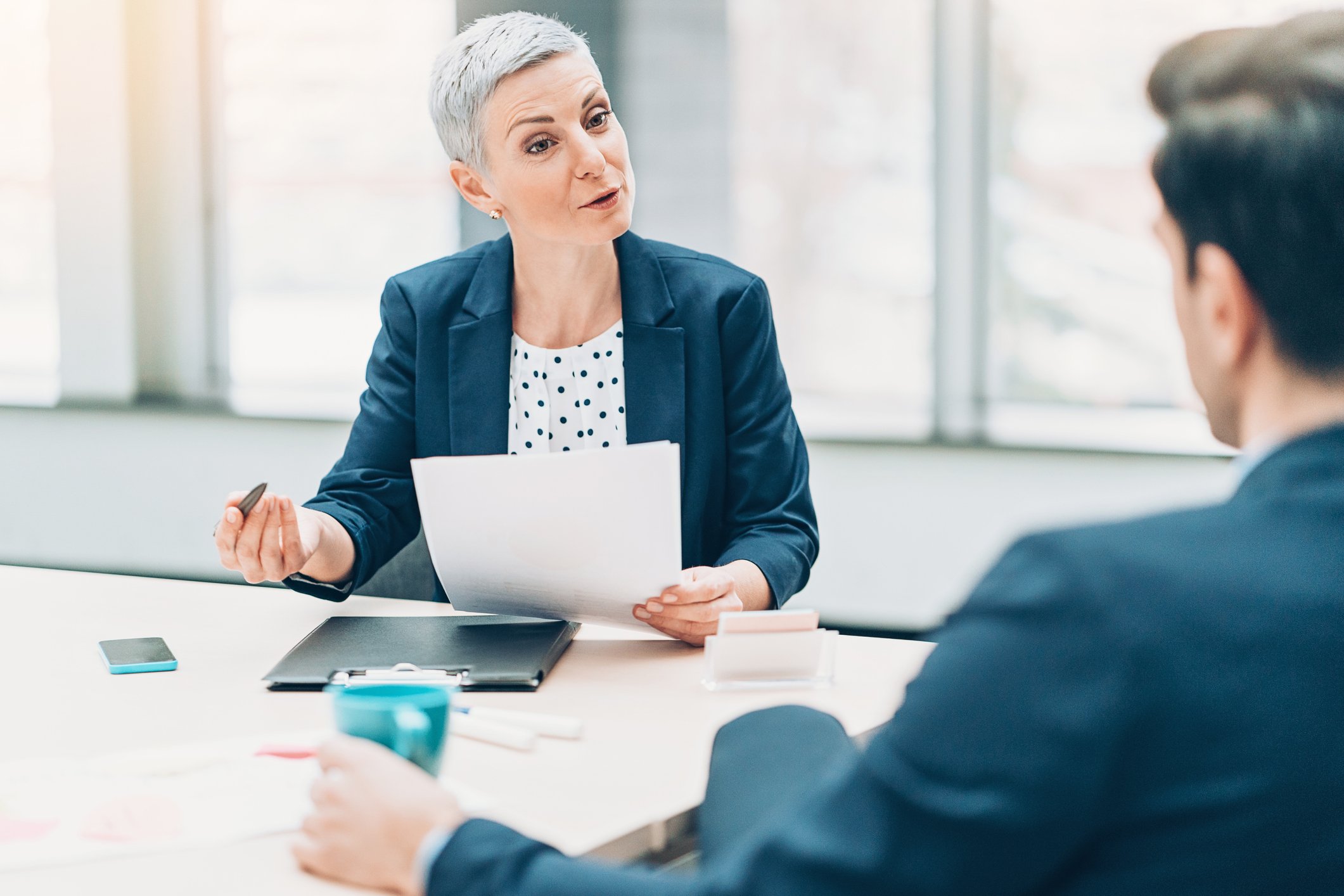 Investor holds a paper while presenting an idea to another investor in a conference room.