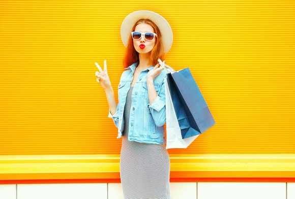 A shopper makes a peace sign while holding two shopping bags.