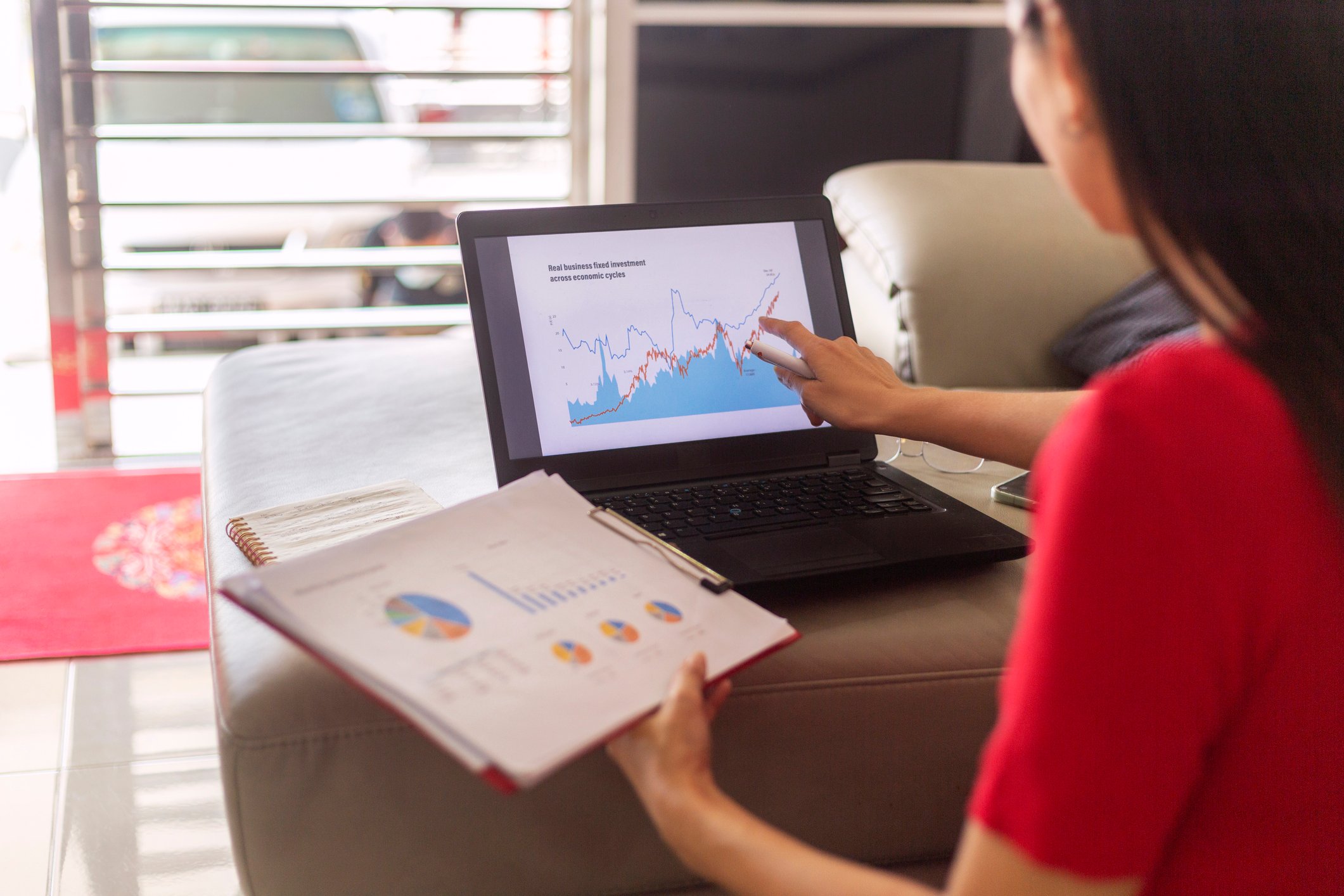 Person conducting financial analysis by reviewing tables and charts on a laptop and a clipboard.