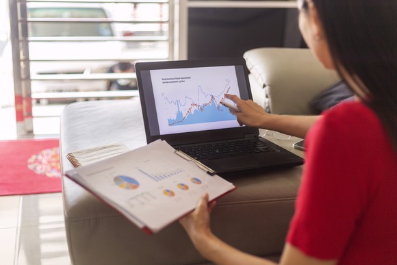 Person conducting financial analysis by reviewing tables and charts on a laptop and a clipboard.