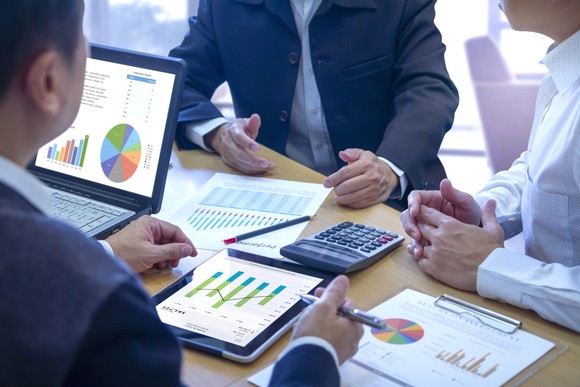 Three people sitting around a table and looking at charts.