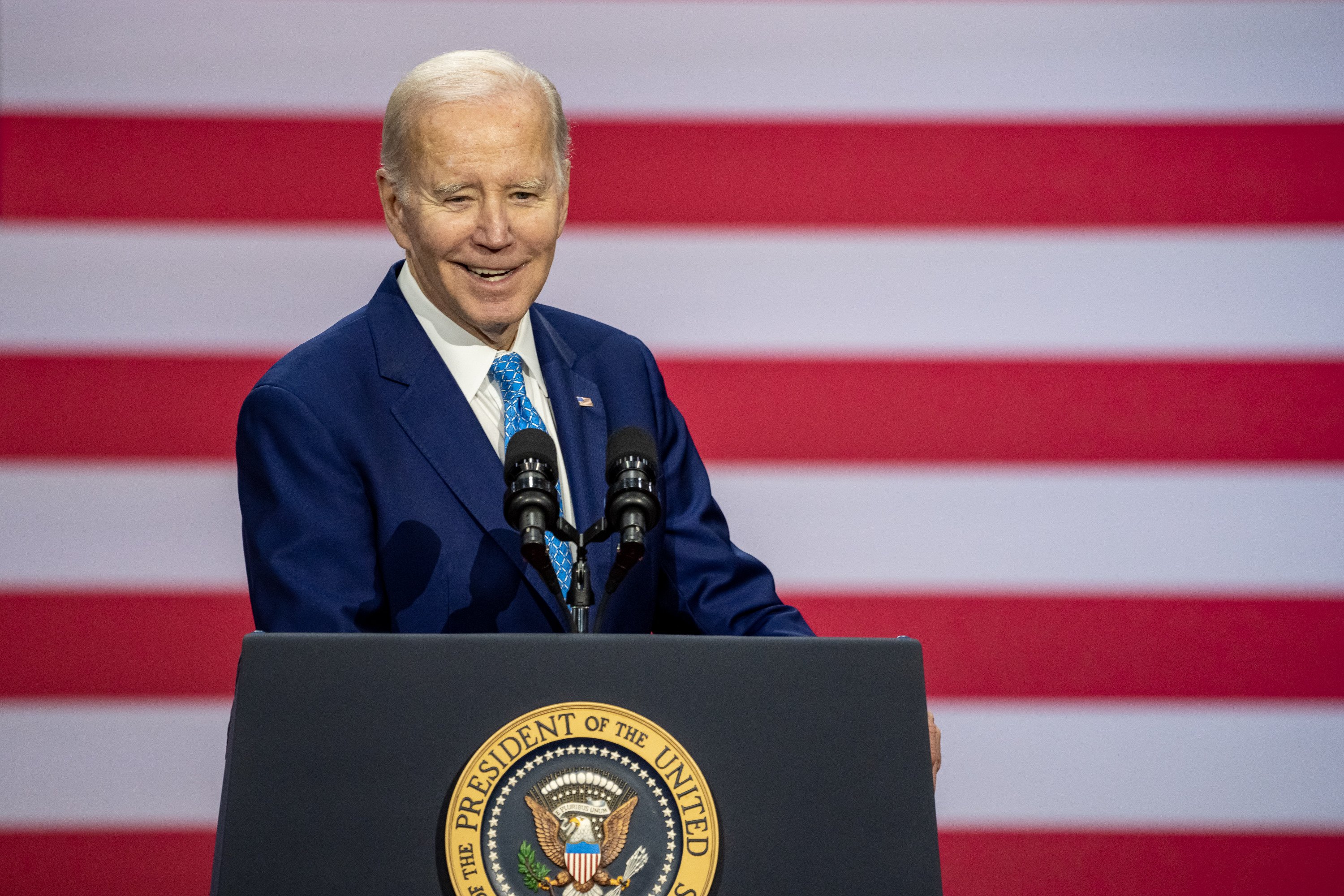 A smiling Joe Biden delivering remarks from behind the presidential podium.
