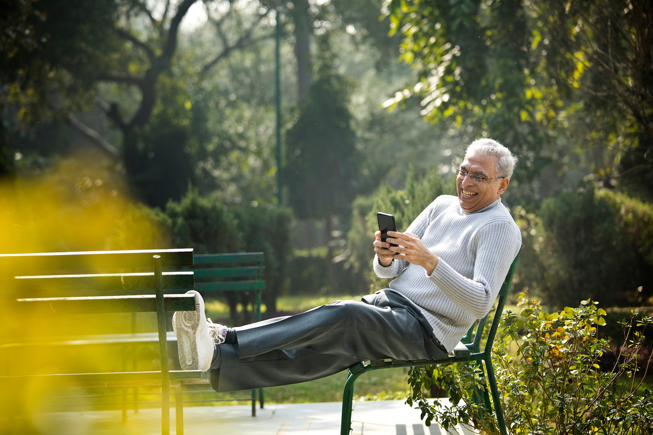 A person smiles while sitting in a park and looking at a phone.