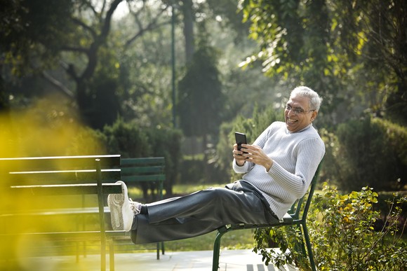 A person smiles while sitting in a park and looking at a phone.