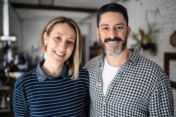 A couple is standing indoors, smiling at the camera.