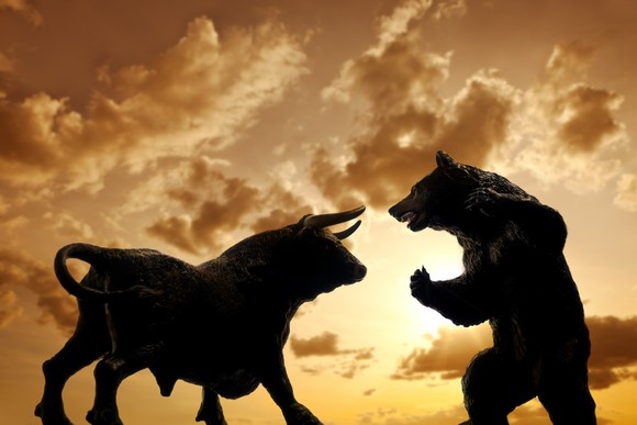 A bull figurine and bear figurine face off against a golden skyline.