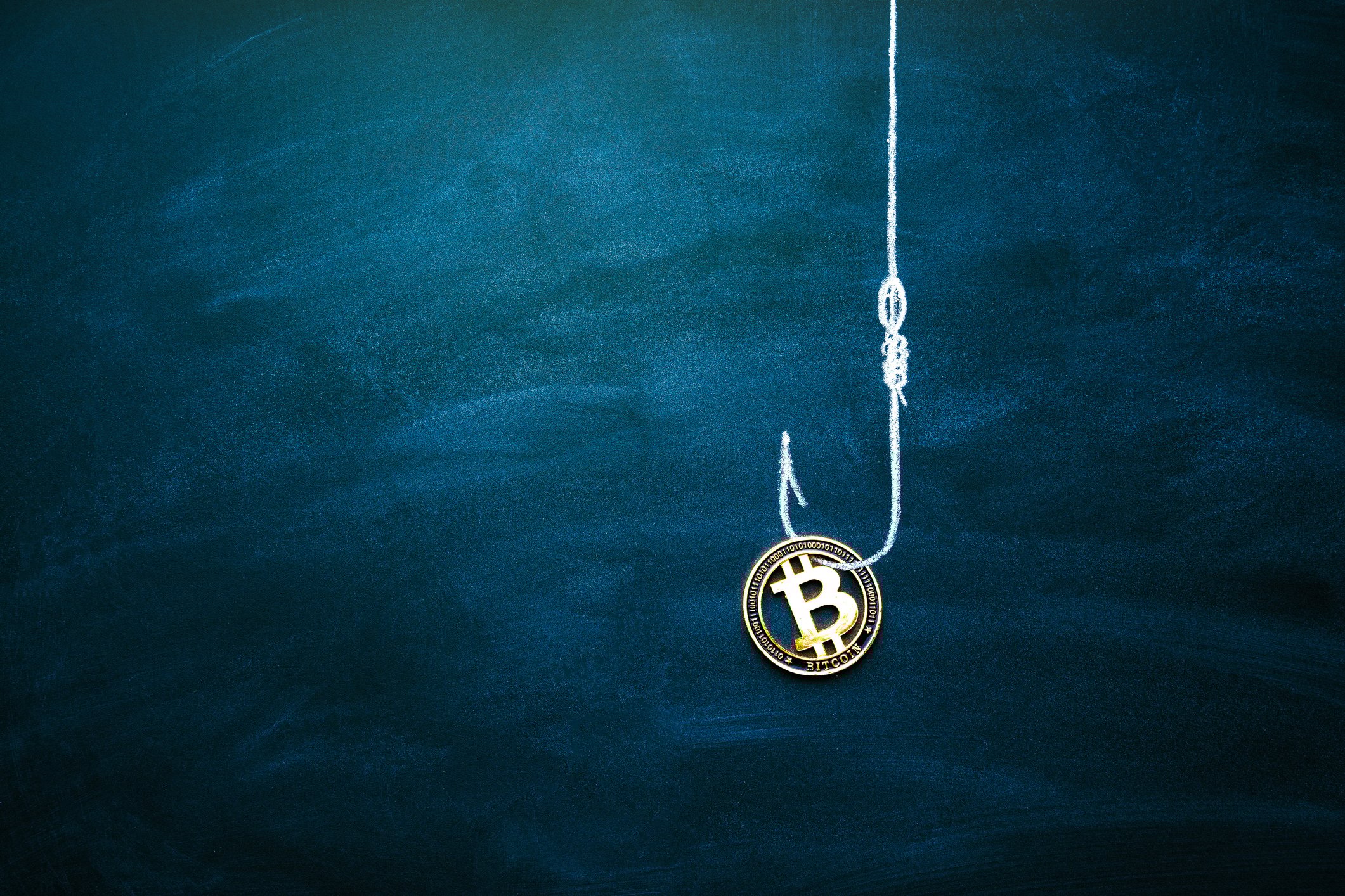 A fish hook holding a coin with the Bitcoin symbol on it.