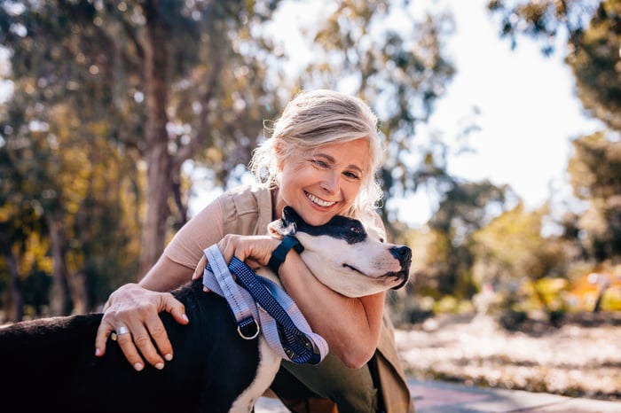 A person is outdoors, squatting and hugging a dog.