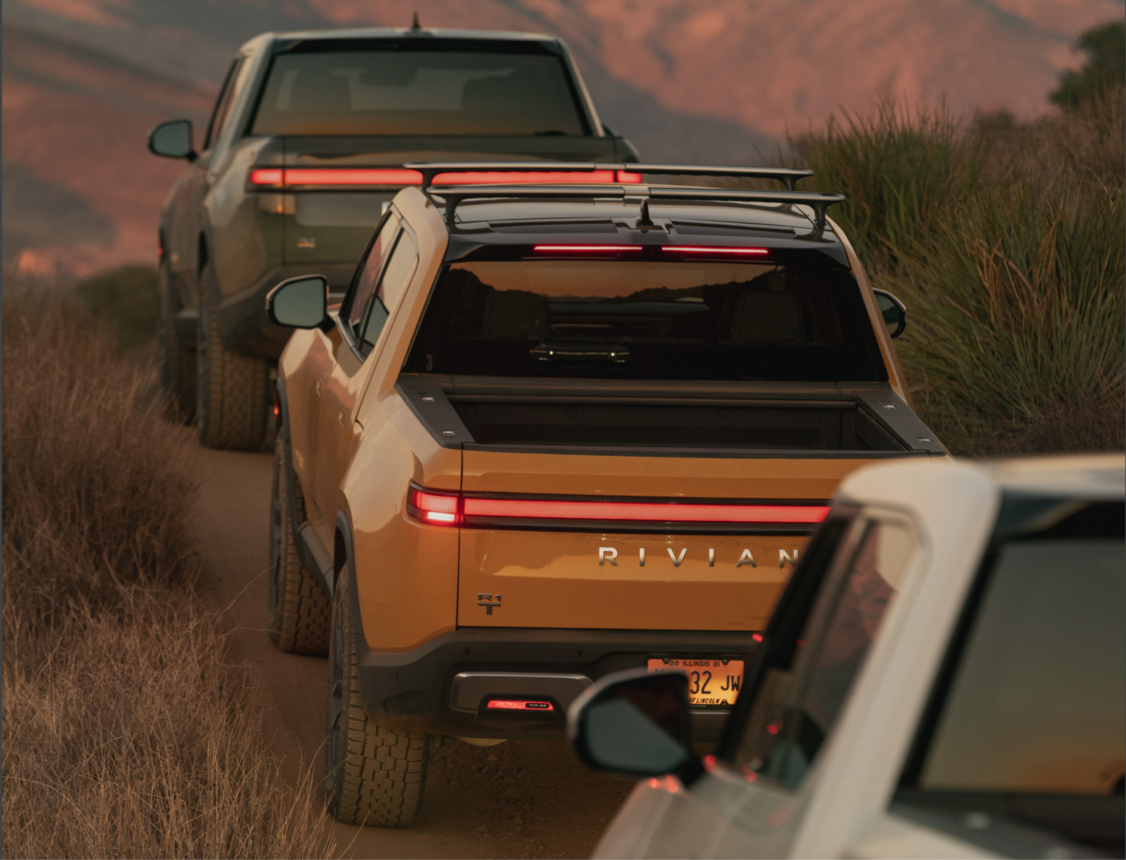 Rivian R1T pickup trucks on off-road trail.