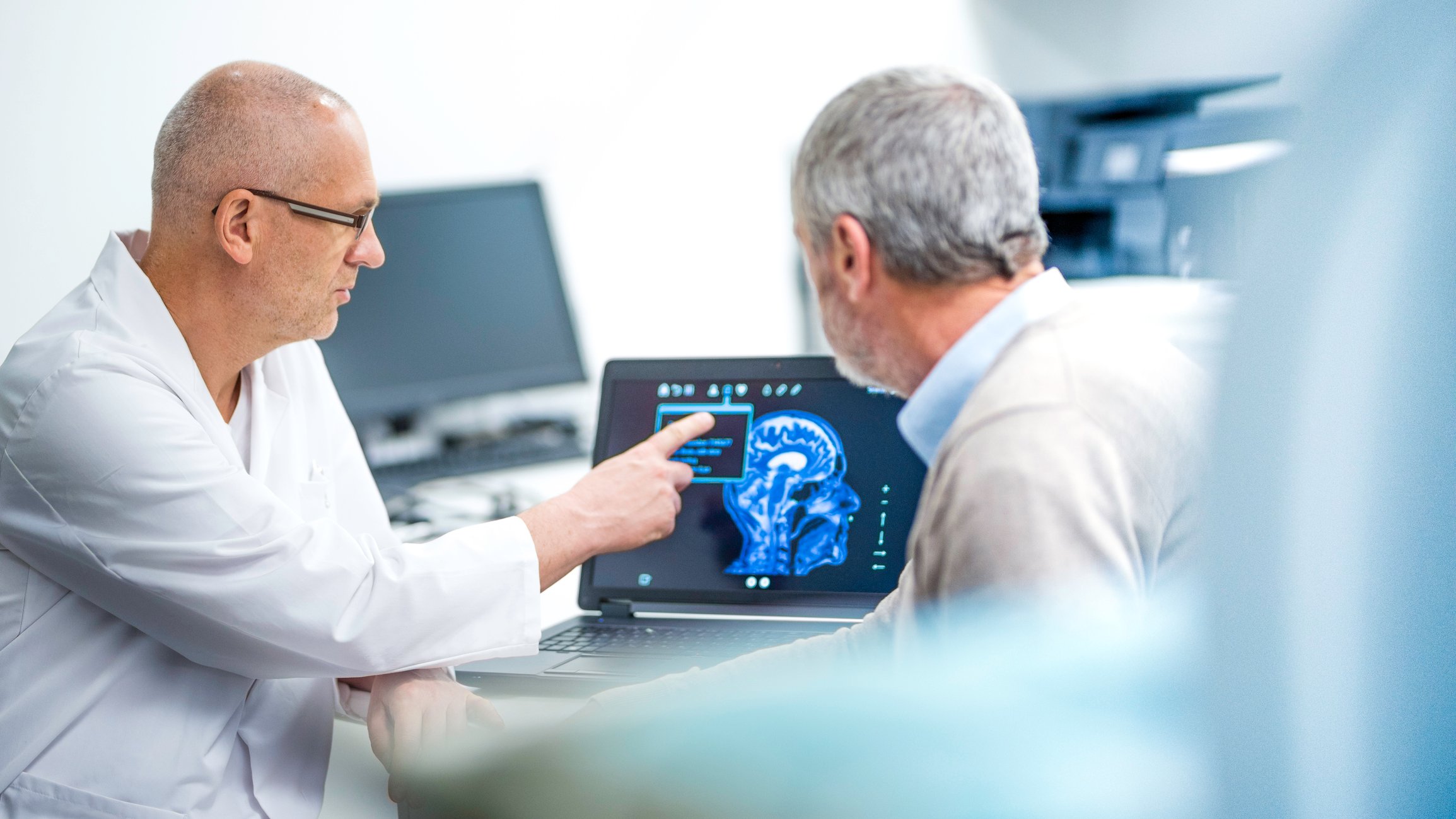 A doctor points to a brain scan while explaining it to a patient.