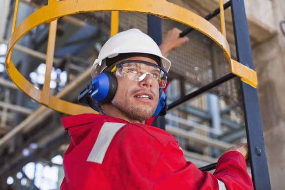 A person wearing a hard hat and personal protective equipment climbs a ladder. 