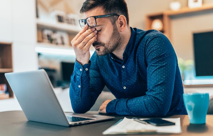 Stressed person with hand on head sitting at desk.