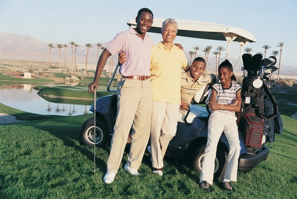 A family posing on a golf course in their golf kart.
