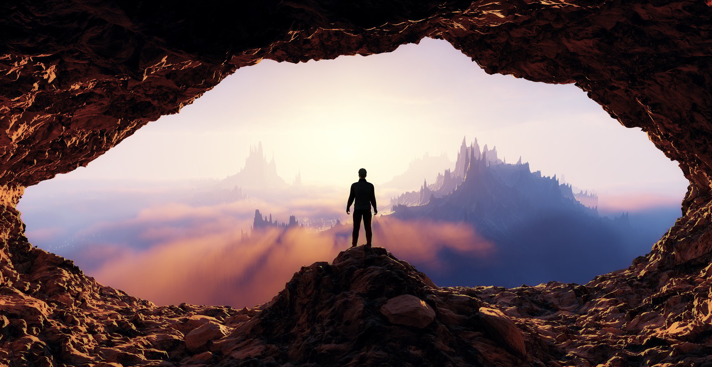 A person stands in a cave overlooking a rocky mountainous landscape.