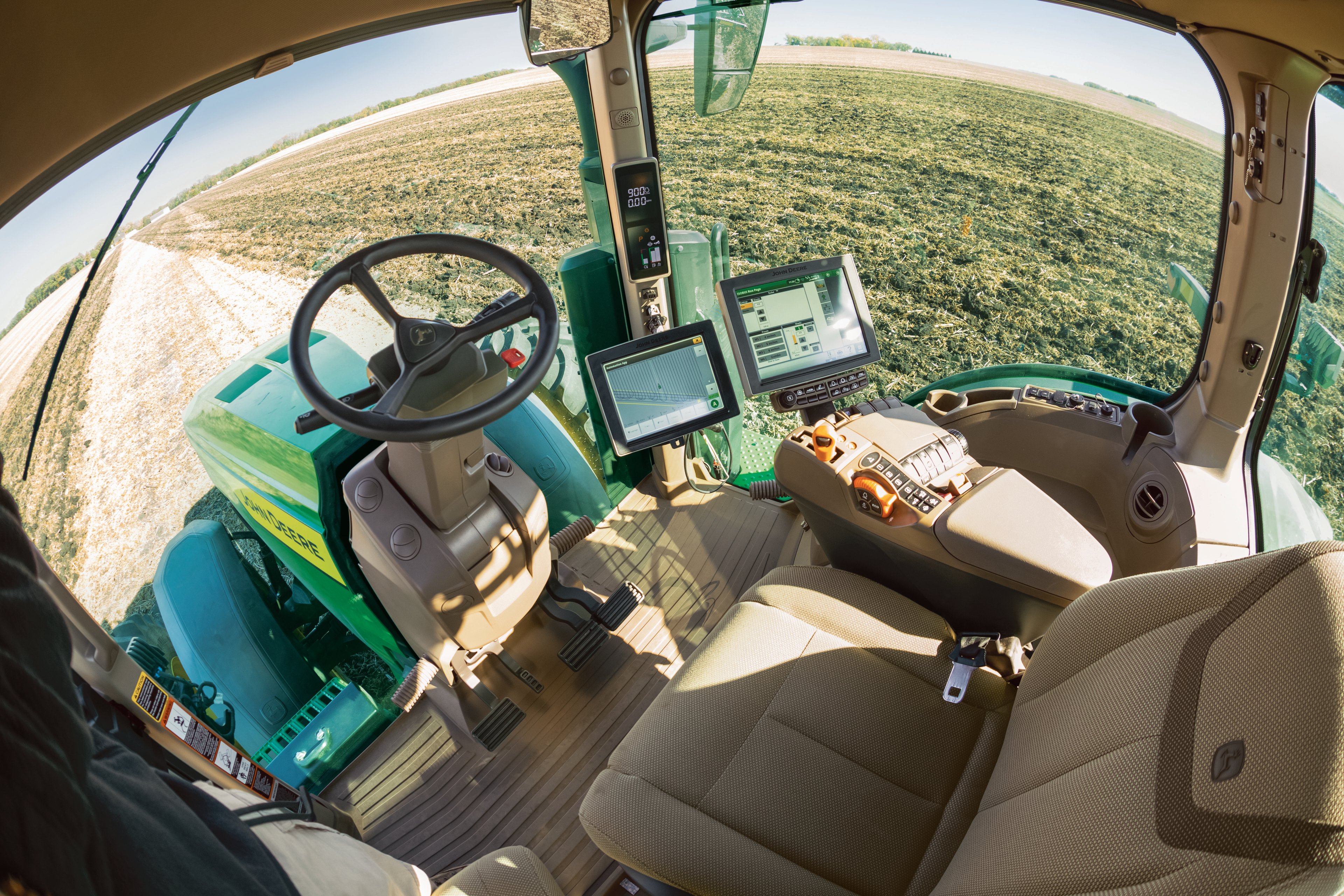 The cockpit of a Deere tractor is seen, including screens used in automation or the tractor's operation