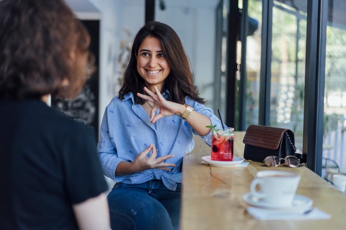 Two seated people are conversing in a coffee shop.