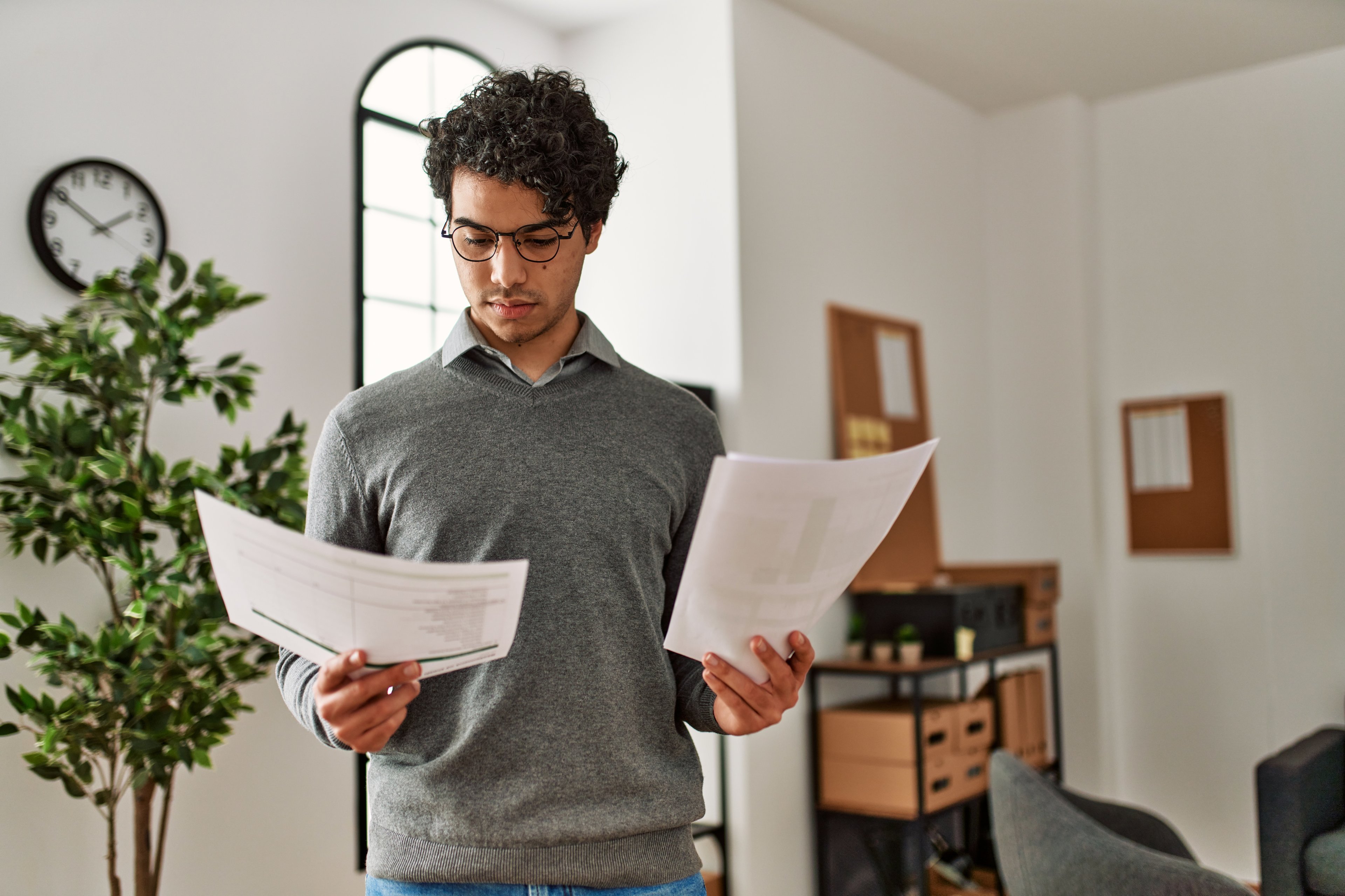 Someone standing up holding two pieces of paper in both hands and looking at one.