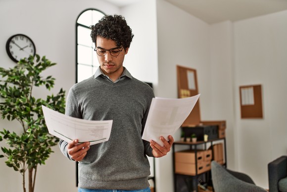 Someone standing up holding two pieces of paper in both hands and looking at one.