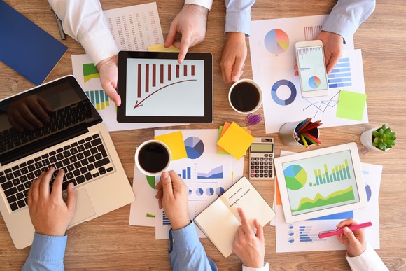 Several pairs of hands around a table holding charts and graphs.