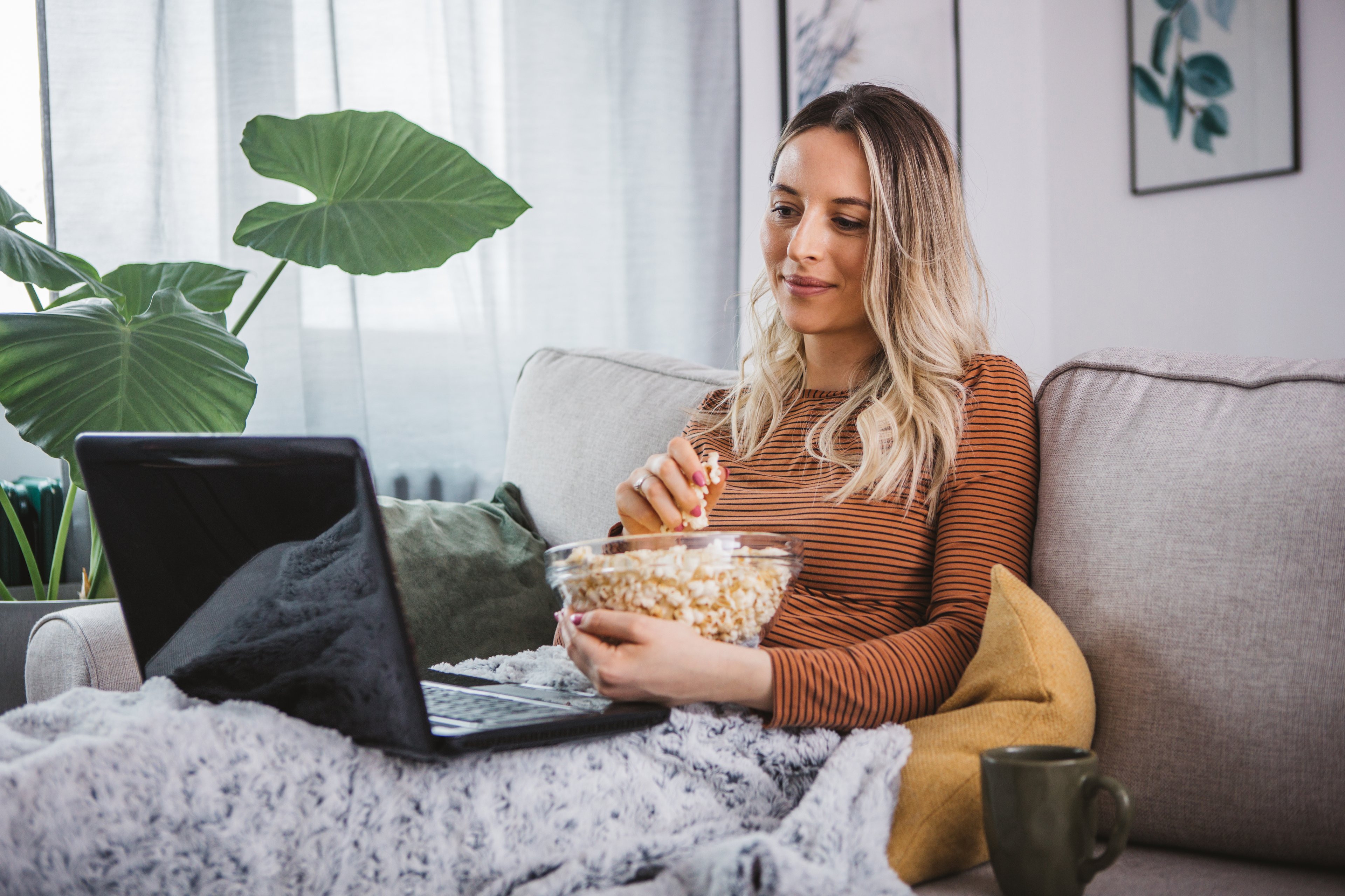 A person streaming a video on their laptop and eating popcorn.