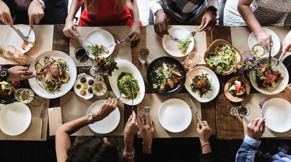 Several people serve themselves at a table with multiple dishes of food on it.