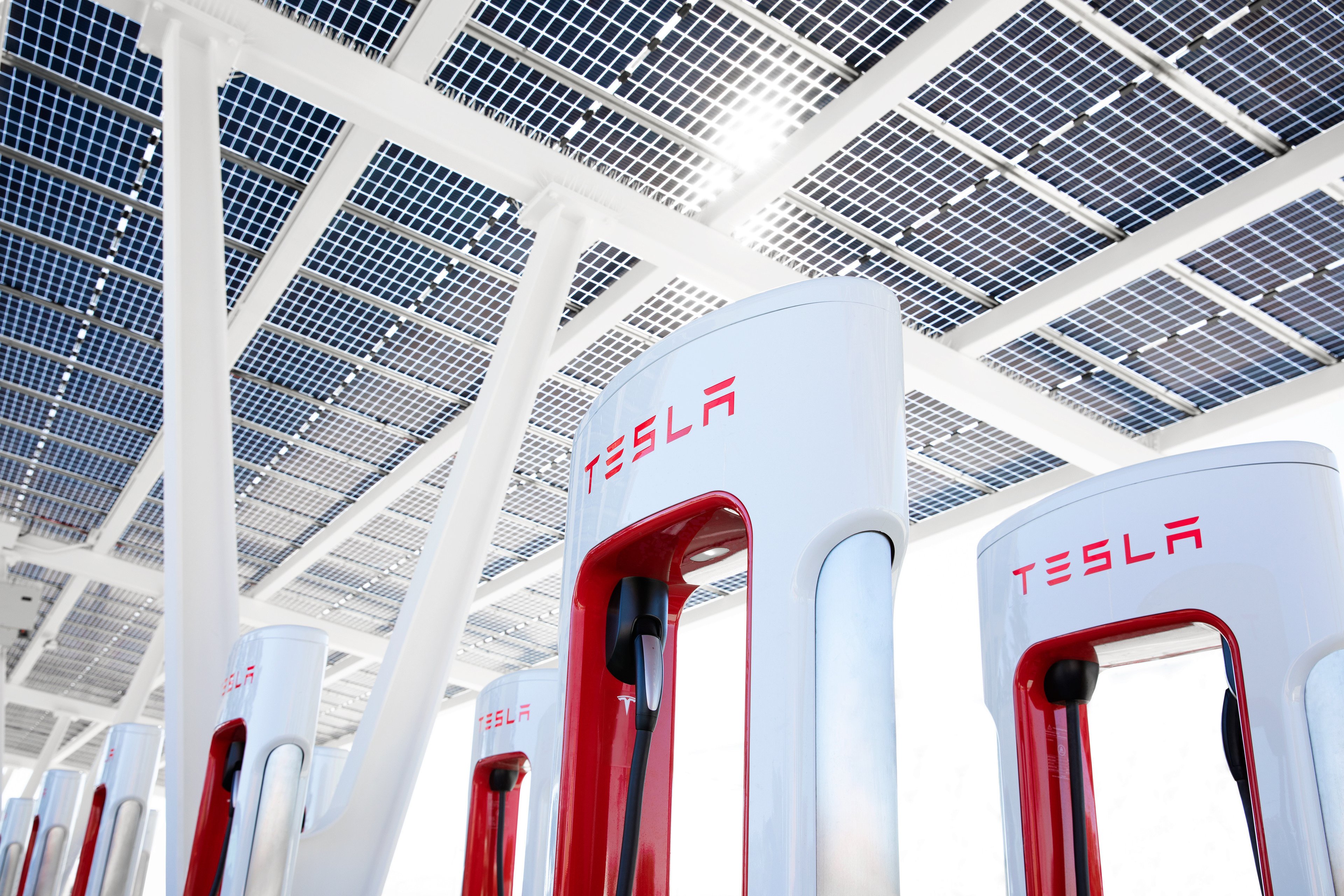 A bank of Tesla EV chargers under a solar-panel-laden roof. 