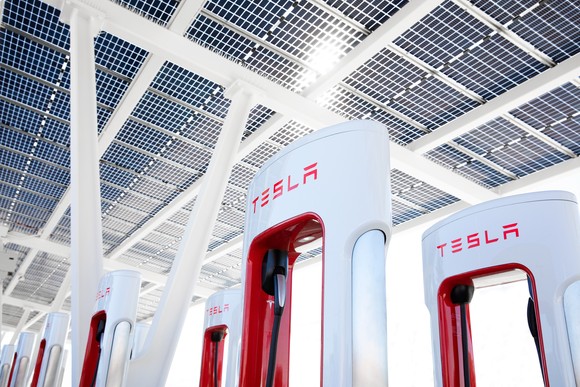 A bank of Tesla EV chargers under a solar-panel-laden roof. 