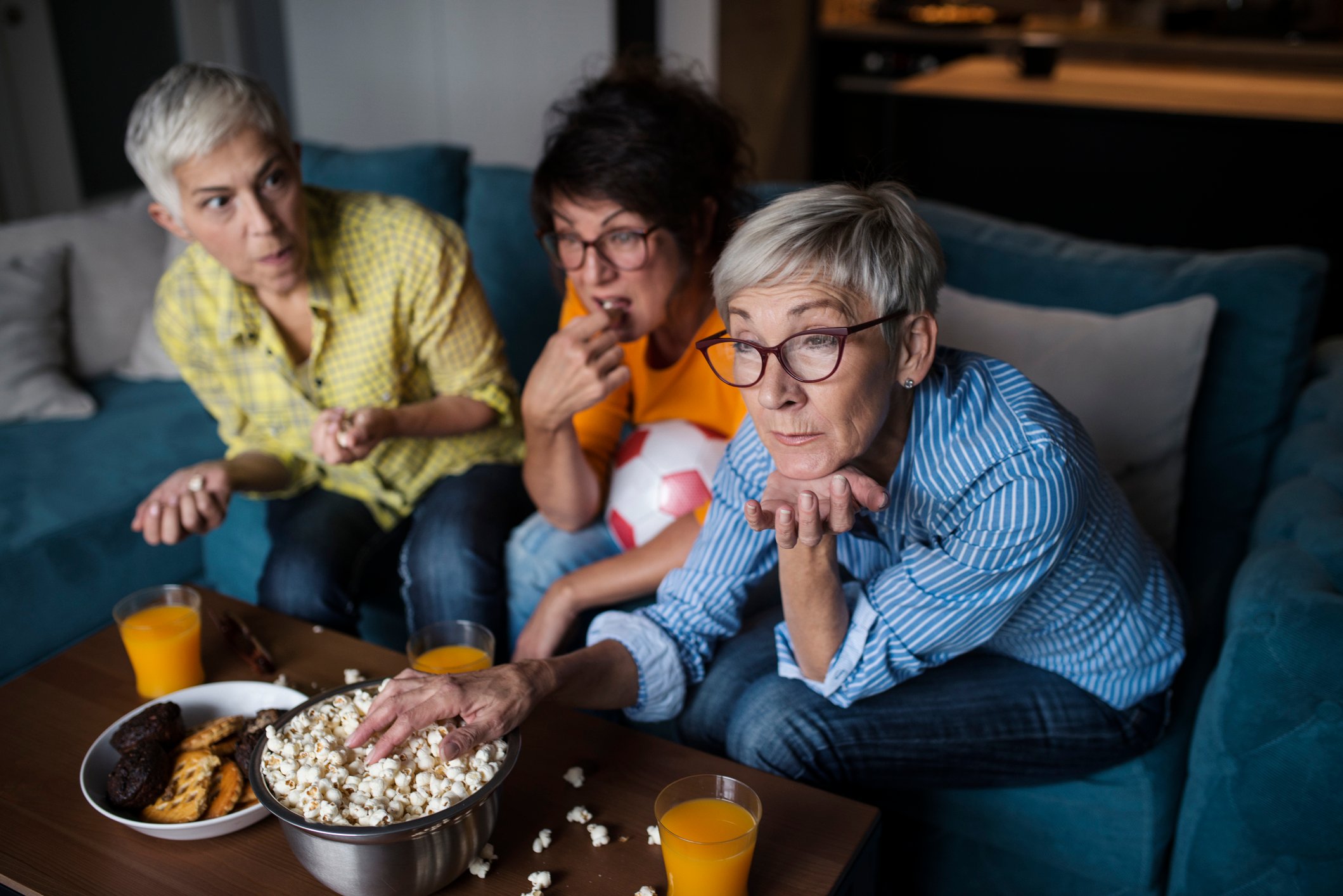 Friends sharing popcorn on the TV couch.