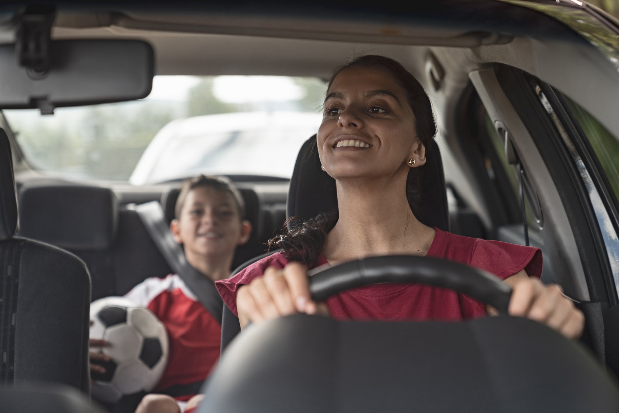 A person driving a child with a soccer ball in a car.
